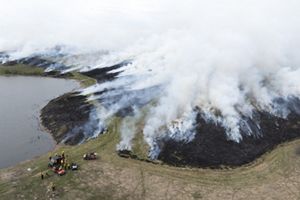 Aerial image of smoke from prescribed fire and people with an ATV standing nearby.