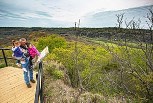 A man holds two young children as they read a sign on the wooden deck at Buzzardroost Rock overlooking the Appalachian hills. 