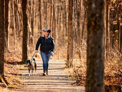 A woman hiking with her leashed dog through a forest.