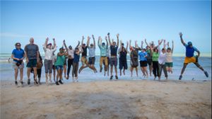 A group of people jump and pose for a photo taken on a beach.