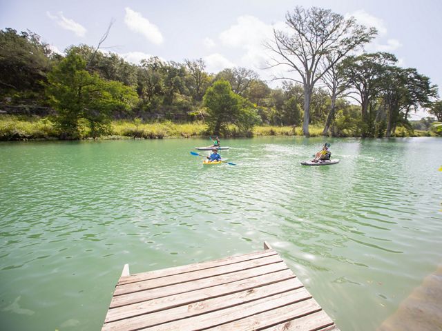 Three people paddle on kayaks down the clear blue waters of a river.
