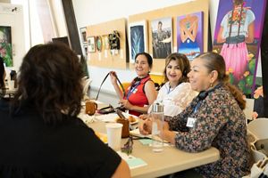 Four people sit together at a table indoors smiling and talking together.