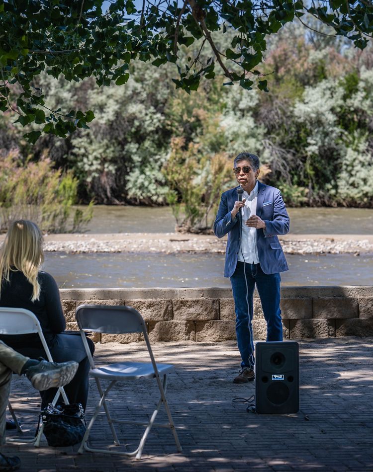 A man speaking to an audience in front of a river.