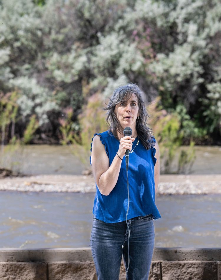 A woman speaking into a microphone in front of a river.