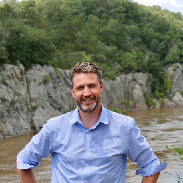 Candid headshot of Tim Purinton standing in front of the Potomac River at the Potomac Gorge.