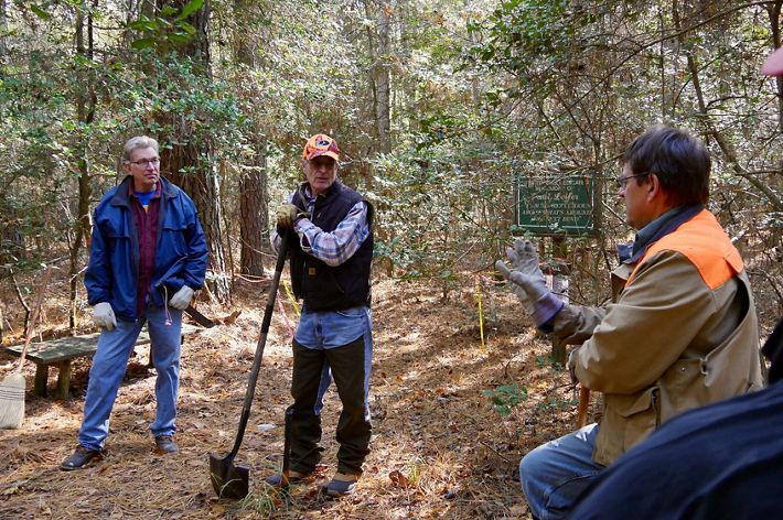 Three men stand in a forest clearing talking during a stewardship workday.