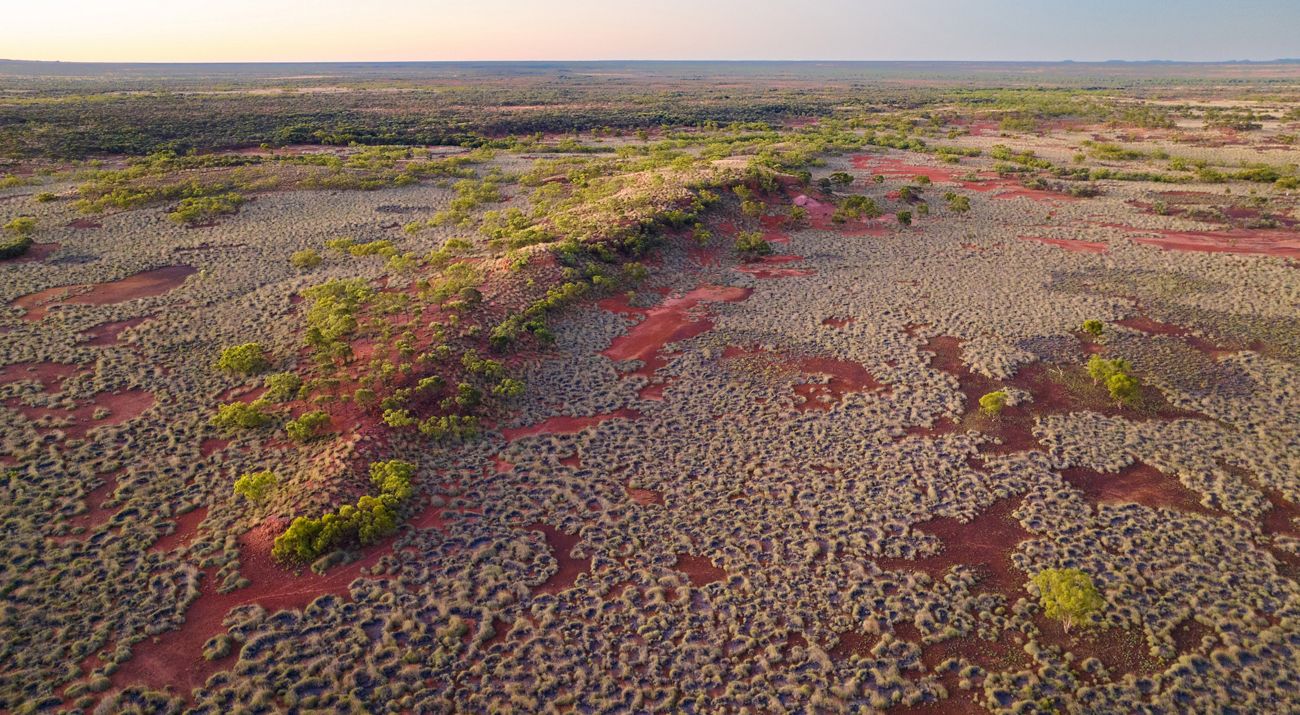 Aerial view of a vast landscape of red earth and scrubby grasses.