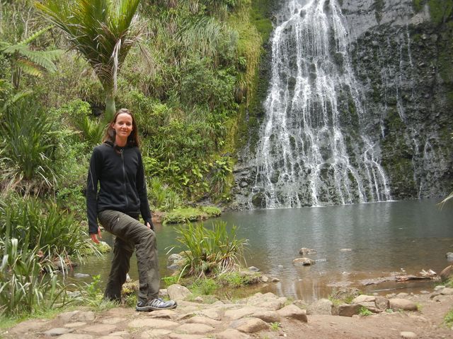 Candid portrait of Chris Arnott, Freshwater Project Manager, standing at the edge of a pool of water. A cascading waterfall is in the background.