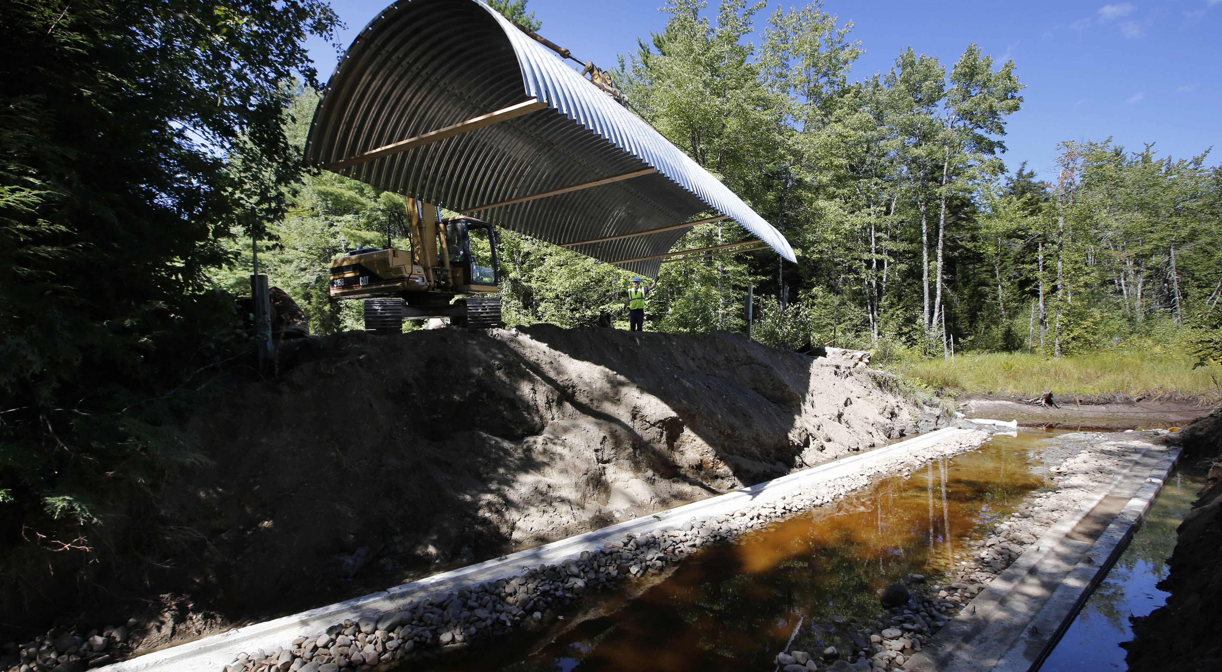 An arch culvert is lowered by backhoe to it's foundations straddling a river in Maine