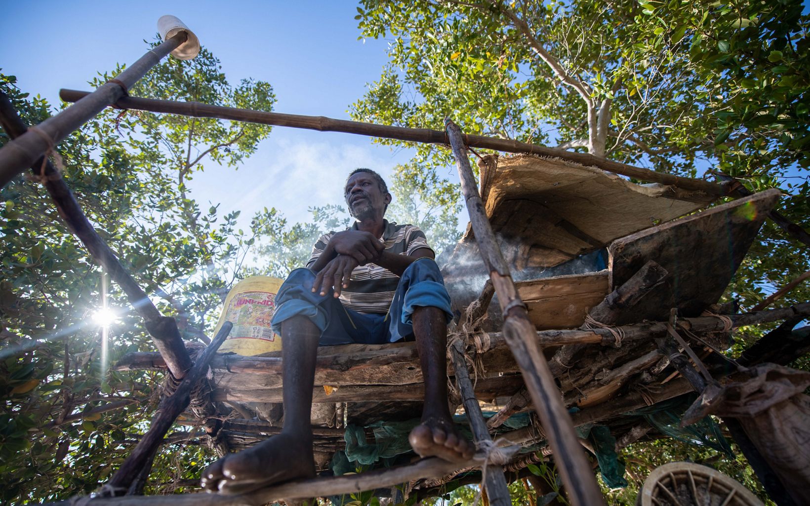 A man sits in an elevated wooden stand with mangrove forests behind him
