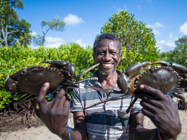 A crab fisherman smiles and holds up two crabs caught from a mangrove forest in Lamu County, Kenya.