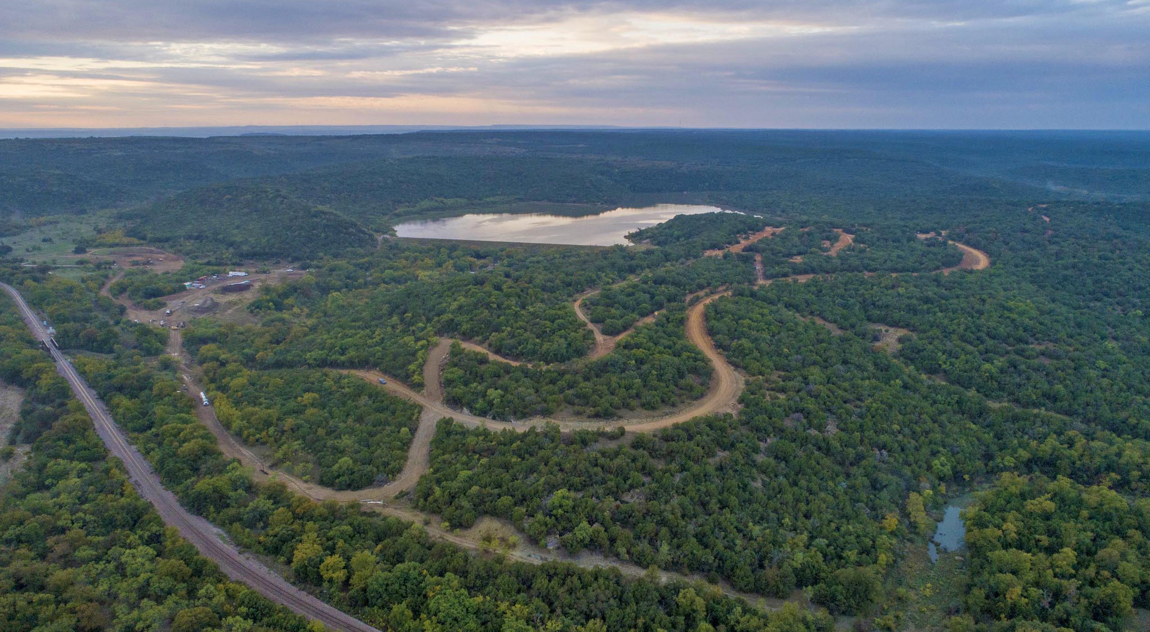 Aerial view of an expanse of green forest and twisting dirt roads with a lake in the middle.