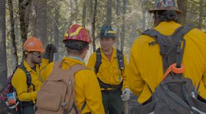 A group of firefighters in training are standing in a circle to learn.