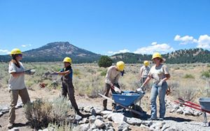 A team of people in hard hats laying rocks along an arid trail.
