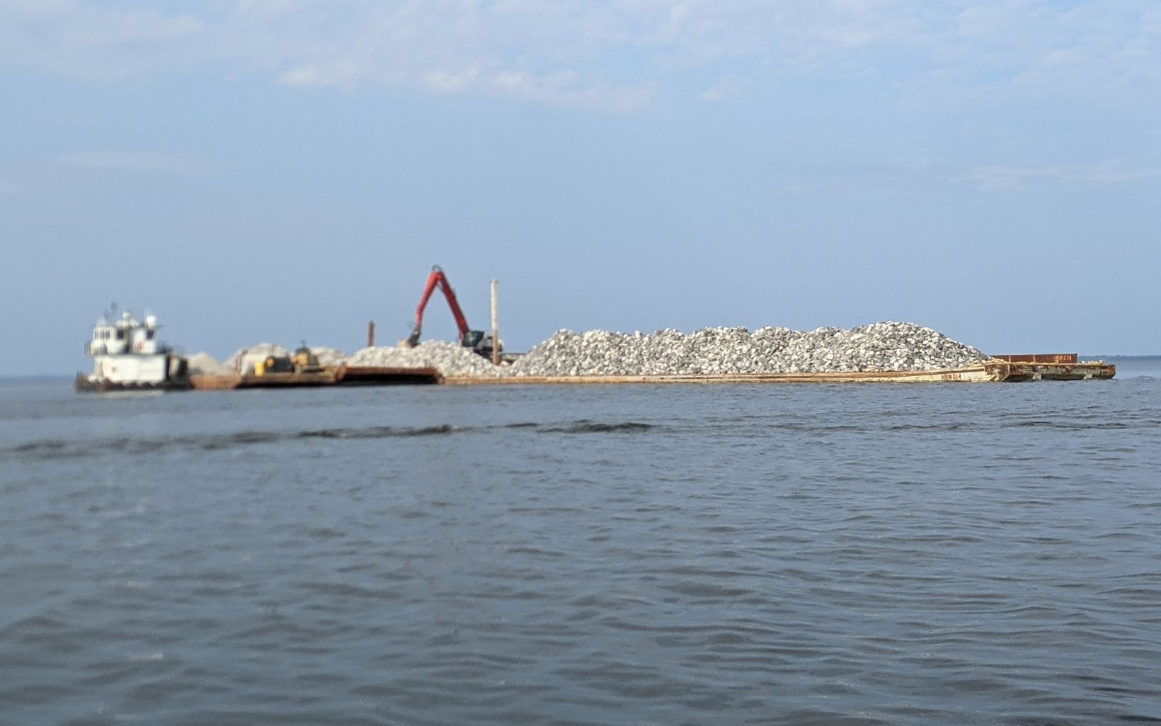 Barge containing limestone rock with an excavator in the bay.