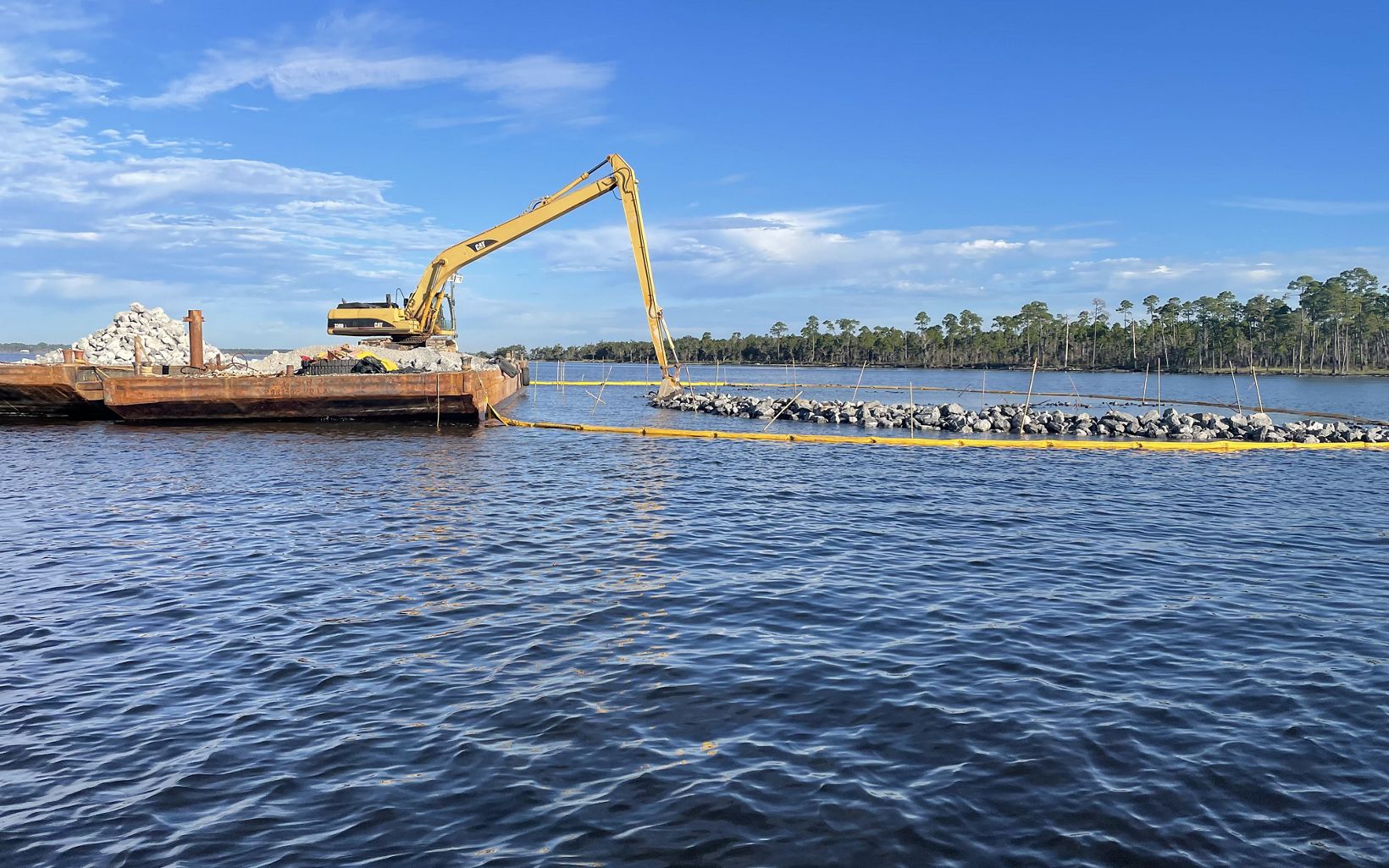 Backhoe sitting atop a barge near an oyster reef under construction.