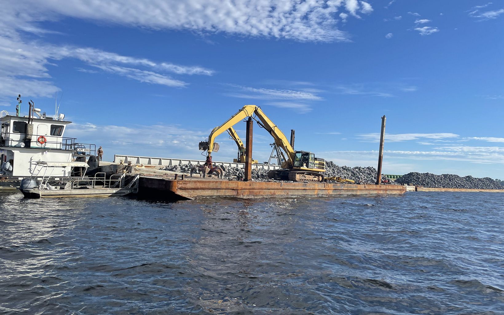 Backhoe sits atop a barge loaded with limestone rock for oyster reef construction.