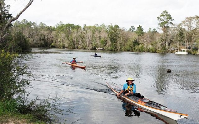 Three men in kayaks enjoy paddling and kayaking on the wide Perdido River in Florida.