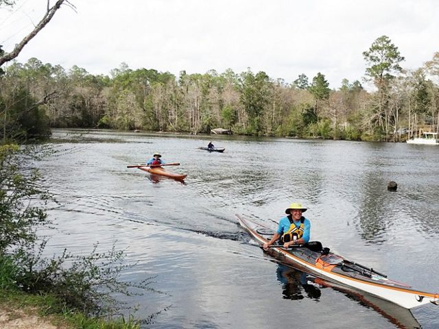 Three men in kayaks enjoy paddling and kayaking on the wide Perdido River in Florida.