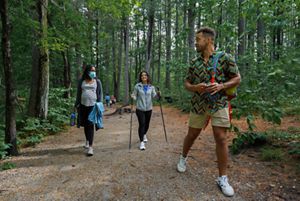 Three people hike on a flat trail in the woods.
