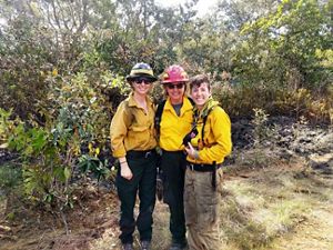 Three TNC staff members who are participating in fire training wear protective fire gear and stand together while smiling at the camera. 