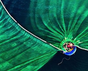 Overhead view of a man on a boat casting a wide, green net.