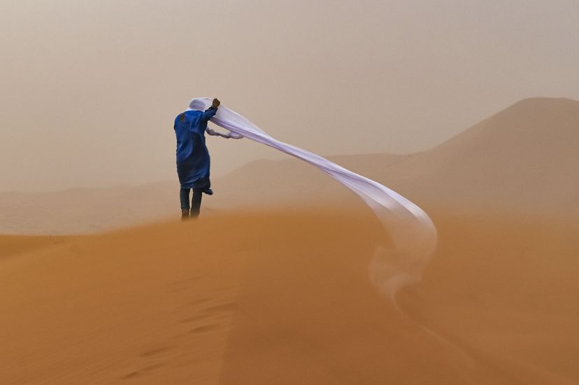 A guide in the Sahara Desert during a sand storm. The person's long, unraveled head wrap blows to the side into the sand.