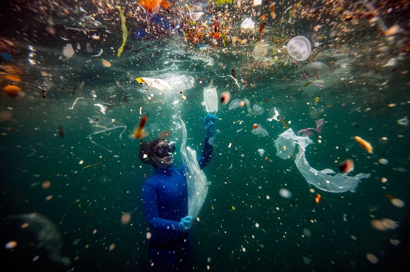 An underwater view of a swimmer completely surrounded by trash, some of it medical waste due to Covid-19.
