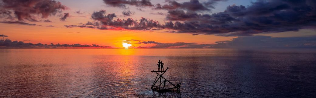 Two people stand on a platform in the ocean at sunset.