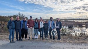 Nine staff members from The Nature Conservancy stand arm in arm in front of a peatland in North Carolina.