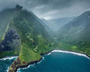 Steep, rugged mountains rise abruptly from the sea, surrounding a secluded lush green valley.