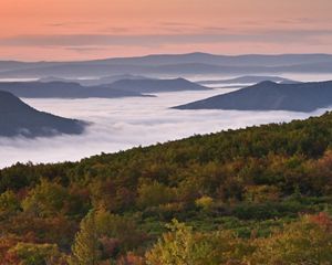 A view of misty mountain tops against an orange-and-pink sky.