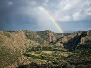 A rainbow in the sky with a canyon below.