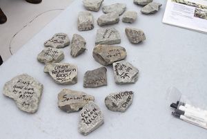 Small rocks are spread out on a table. The rocks have messages written on them include, "Oyster Restoration Rocks!".