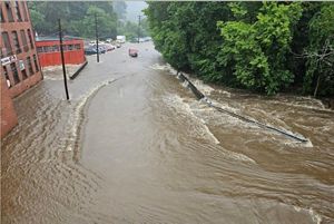 Brown floodwaters flow down the street of a town.