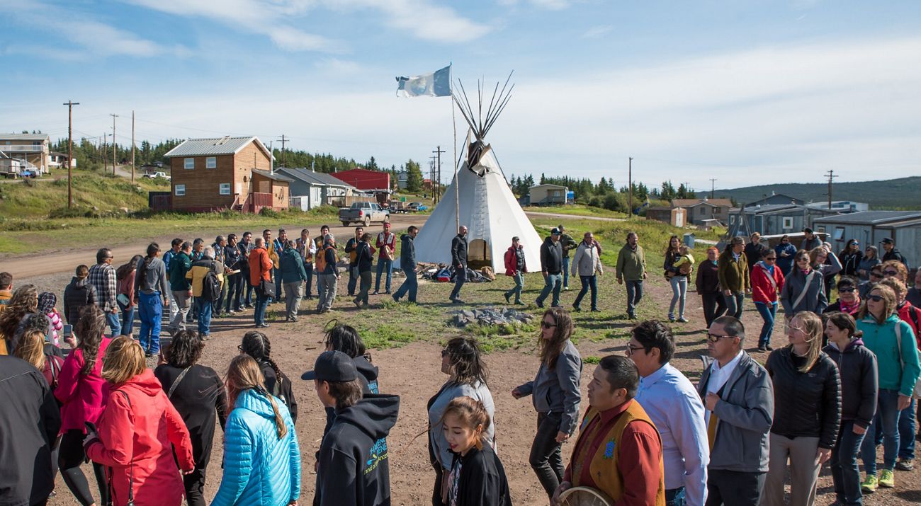 a group of people walk in a circle around a fire on a sunny day in northwest territories.