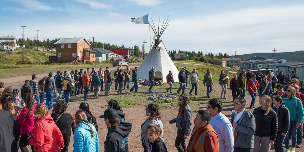 a group of people walk in a circle around a fire on a sunny day in northwest territories.
