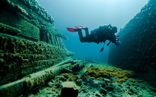 A SCUBA diver swims among concrete and wooden structures in the waters of Lake Huron.