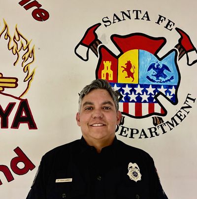 A male firefighter is smiling for a photo in front of the department logo.