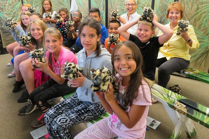 Elementary students smile in a classroom with teachers and chaperones as they hold stuffed animals of baby florida panthers