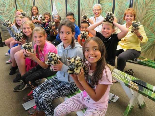 Elementary students smile in a classroom with teachers and chaperones as they hold stuffed animals of baby florida panthers