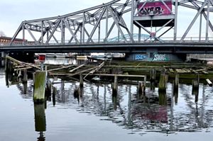 Rotting timbers emerge from the water with a steel-framed swing bridge in the background on a cloudy winter day.