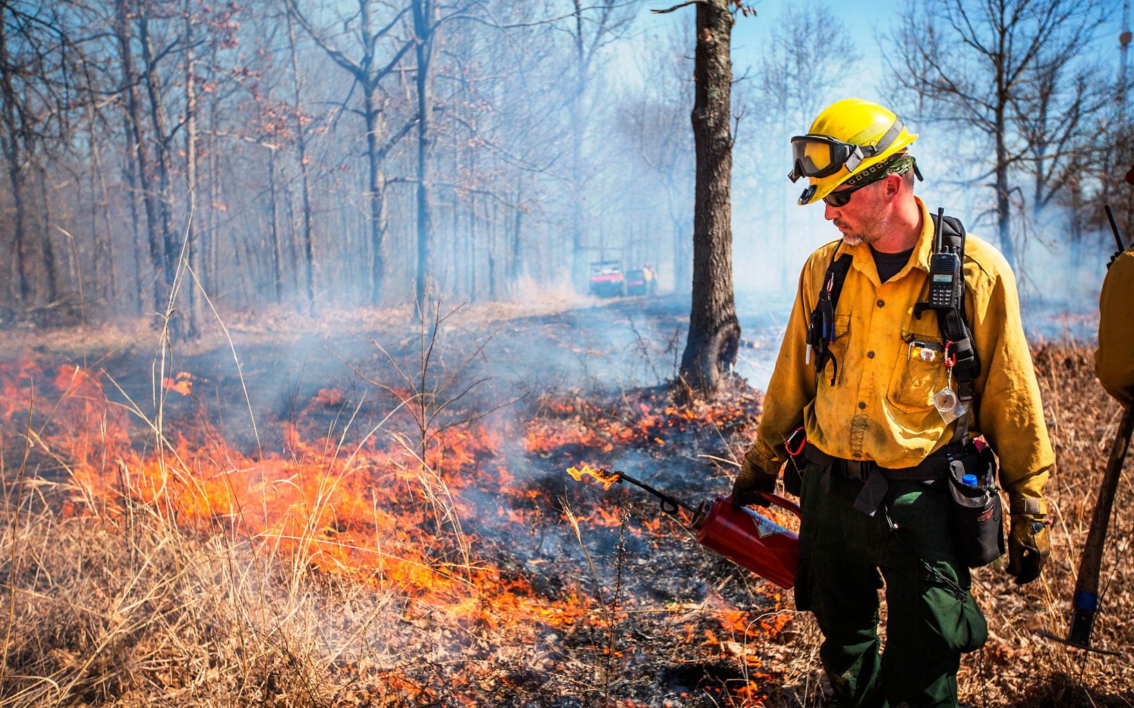 A man with a yellow helmet follows a fire.