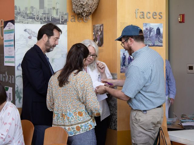 Four attendees at the Coastal Relocation Workshop stand in front of a wood paneled wall bent over a piece of paper, mid-discussion.