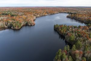 Aerial photo of a small pond surrounded by pine and oak forest during fall foliage season