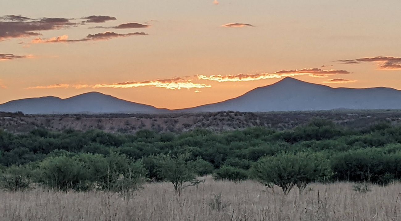 Landscape of a grassland leading out to rolling hills and a sunset.