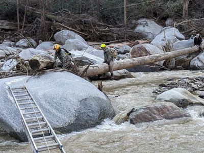 People crossing a river by crawling along a log.