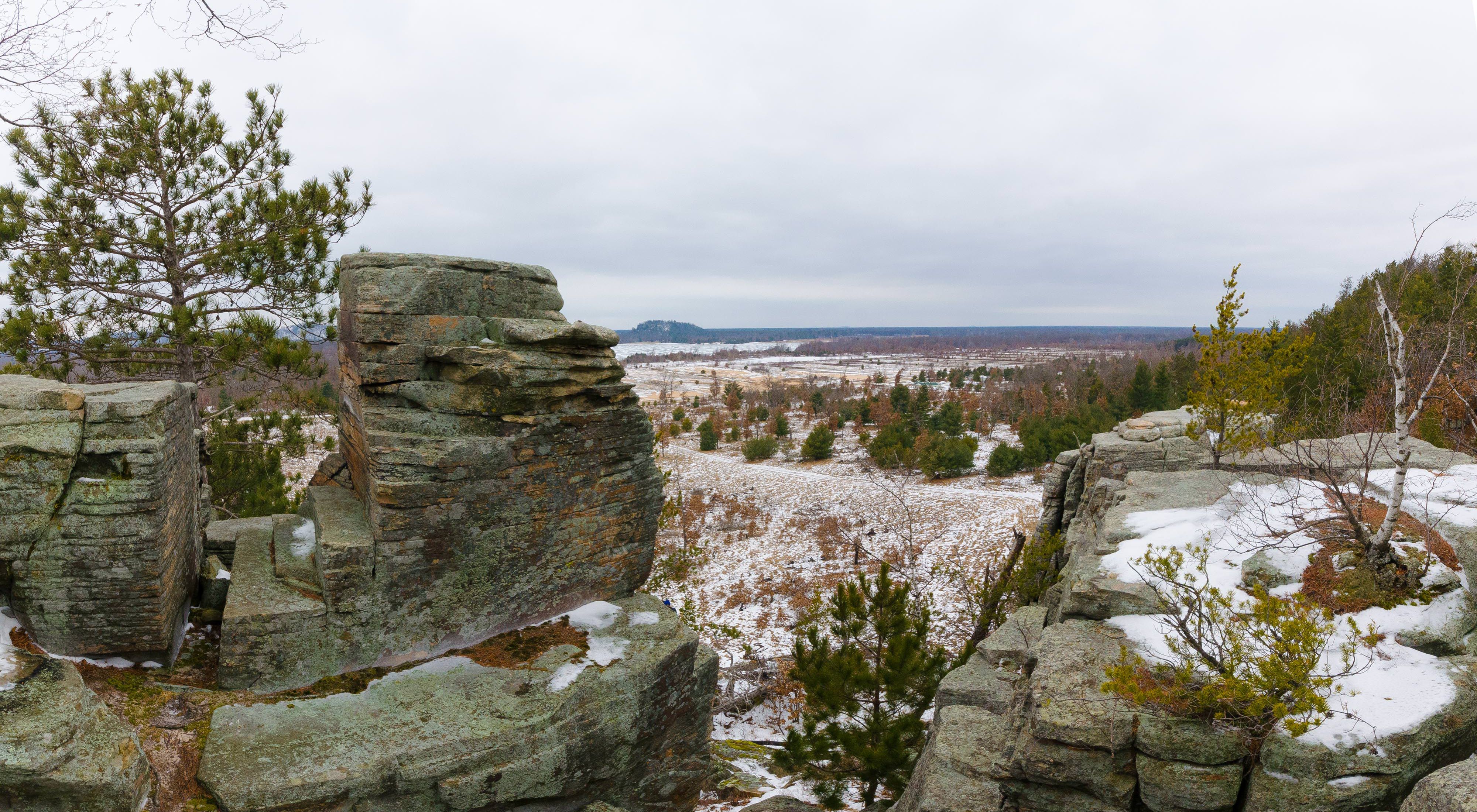 Panoramic view over the wintry landscape from the rocky, snow-covered bluffs dotted with birch and conifer trees at the Quincy Buff and Wetlands State Natural Area.