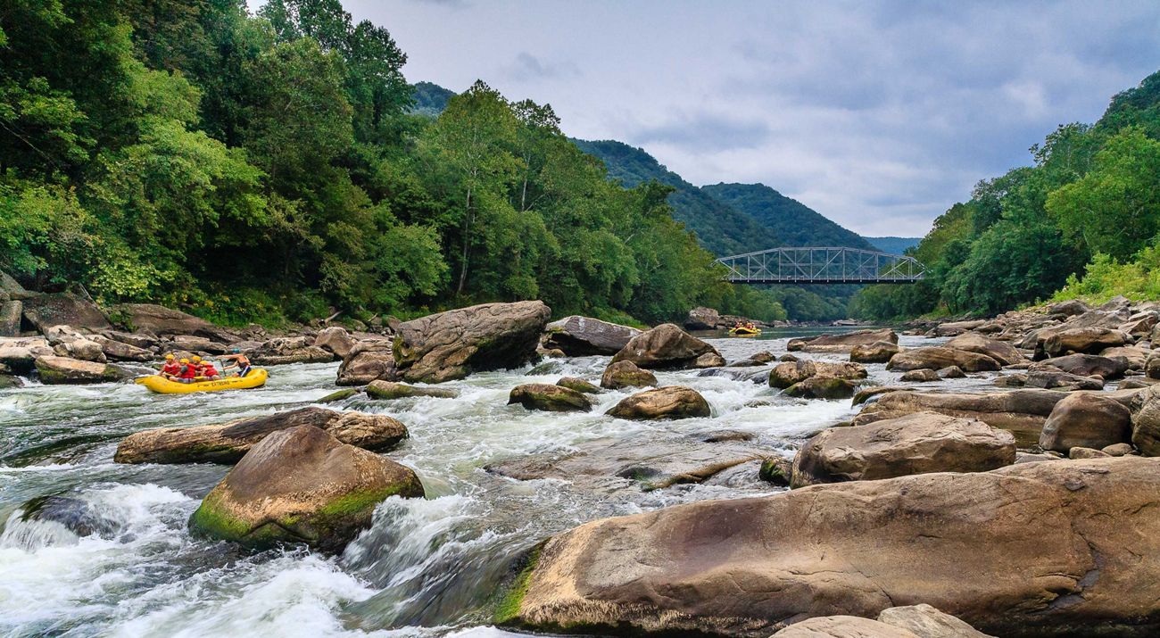people in a whitewater raft exploring a rocky river with a bridge in the distance