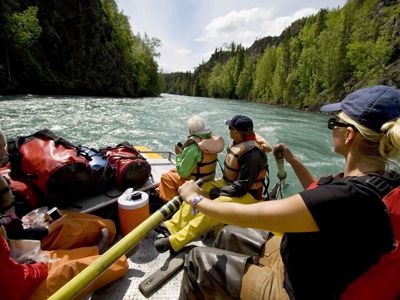 Two people and a guide sit in a whitewater raft and travel down a river.